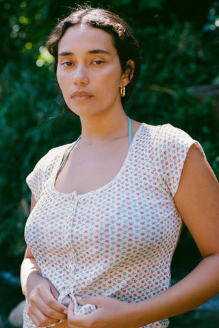 Woman wearing a floral cap sleeve top outdoors with greenery in the background