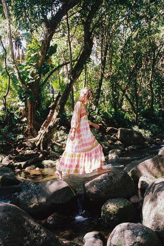 Woman in a colorful dress walking through a forest with rocks and water.