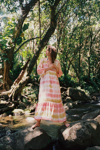 Woman in a colorful dress standing on rocks by a stream in a forest