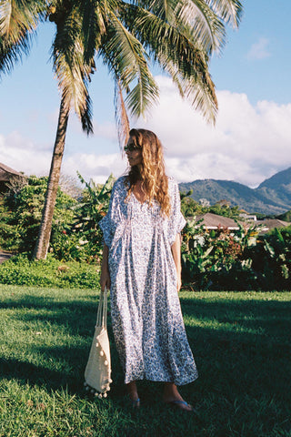 Woman in a floral dress standing under palm trees with mountains in the background