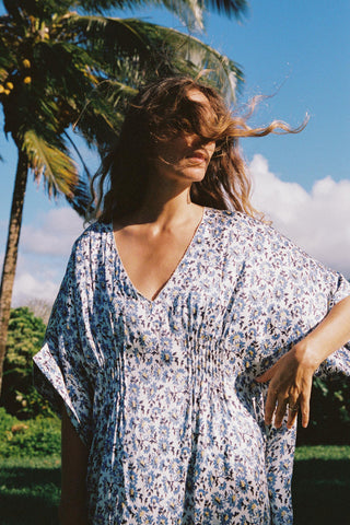 Woman in a floral dress standing outdoors with palm trees and blue sky in the background
