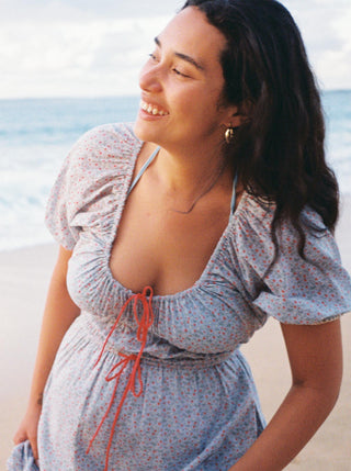 Woman in a floral dress with orange drawstring standing on a beach.