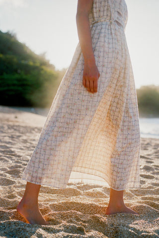 Person wearing a checkered dress standing on a sandy beach with a blurred natural background
