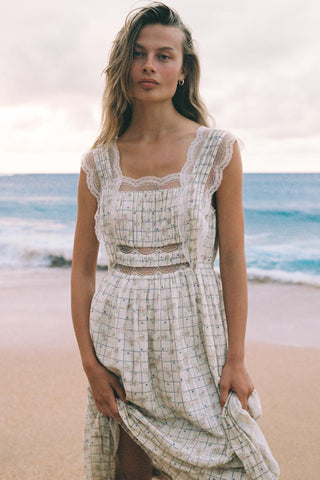 Woman in a white patterned dress standing on a beach with ocean in the background