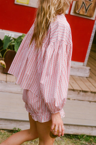 Person wearing a red and white patterned outfit standing in front of a red wall.