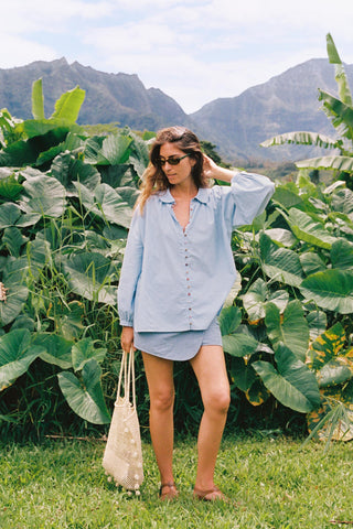 Woman in a light blue outfit standing in a lush green field with mountains in the background