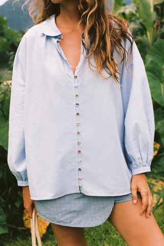 Person wearing a light blue chambray button-up  shirt over a plaid skort in a natural setting