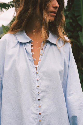 Light blue chambray button-up shirt worn by a person with a blurred natural background