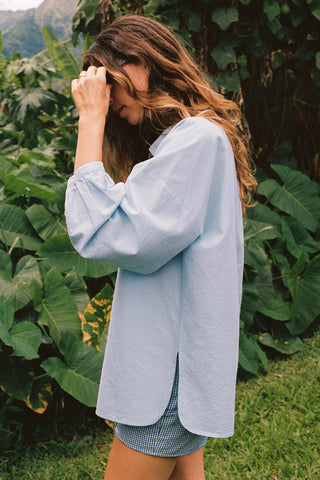 Woman wearing a light blue shirt with rolled-up sleeves in a natural setting