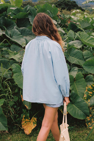 Person wearing a light blue jacket standing in a field of large green leaves.