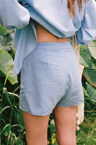 Person wearing blue plaid skort with a light blue top against a green leafy background