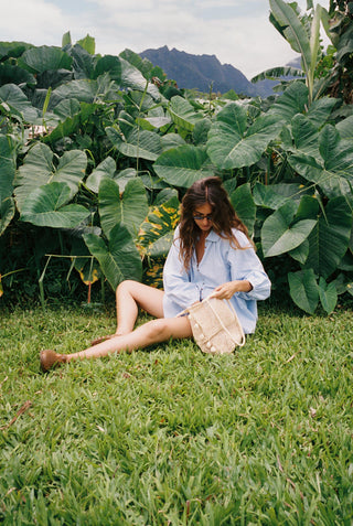 Woman sitting on grass with large green leaves and mountains in the background