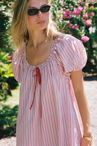 Woman wearing a red and white patterned dress with sunglasses outdoors.