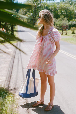 Woman in a red and white striped pattern dress standing on a road with trees in the background
