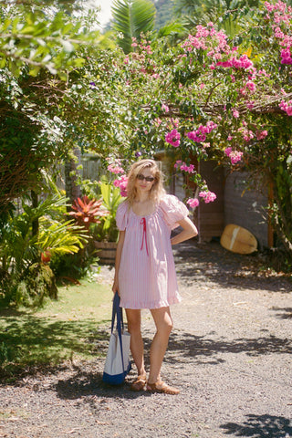 Woman in a red and white striped pattern dress standing in a garden with pink flowers and greenery.