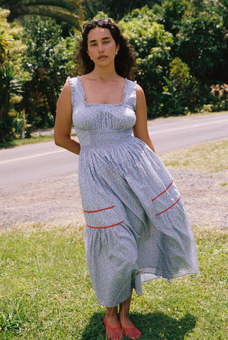 Woman in a light blue floral dress with red trim standing outdoors on grass