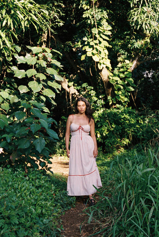 Woman in a red and white striped dress with red trim standing in a lush green forest