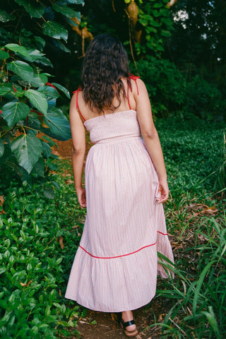Woman in a red and white striped dress with red trim walking through a lush green garden.