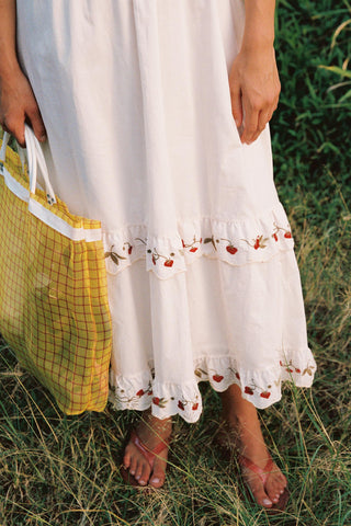 Person wearing a white dress with floral embroidery in a grassy field
