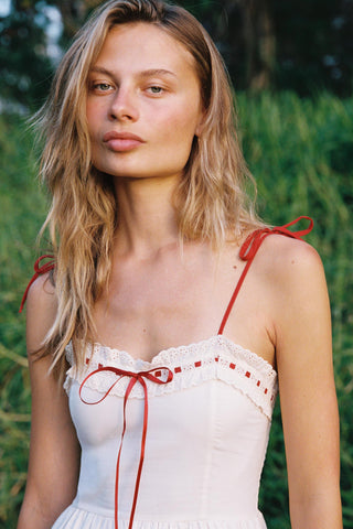 Woman wearing a white dress with red straps against a natural background