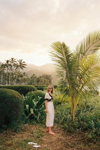 Woman standing in a lush garden with palm trees and mountains in the background