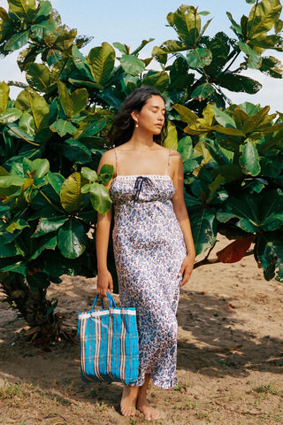 Woman in a floral dress holding a blue bag among large green leaves