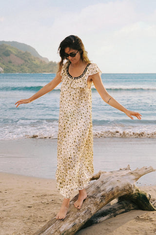 Woman in a long dress standing on a beach with ocean and mountains in the background