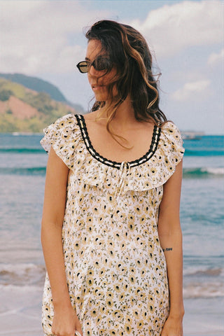 Woman in a floral dress standing on a beach with ocean and mountains in the background