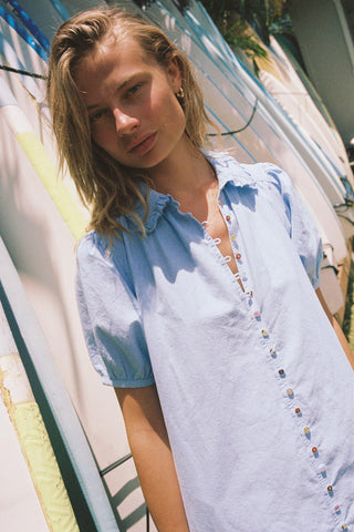 Woman in a chambray button down dress  with surfboards in the background
