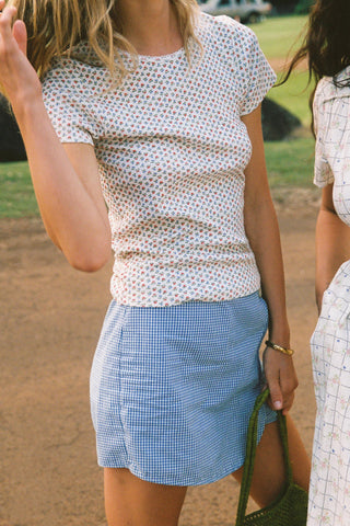 Woman wearing a floral patterned white shirt and blue checkered skort outdoors.