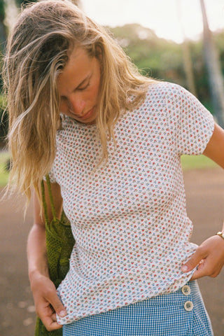 Woman wearing a floral patterned white shirt with a blue skort outdoors