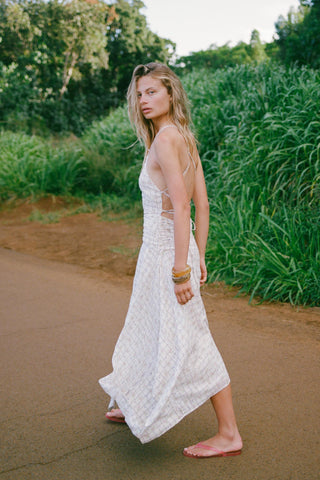 Woman in a white dress standing on a dirt path surrounded by greenery