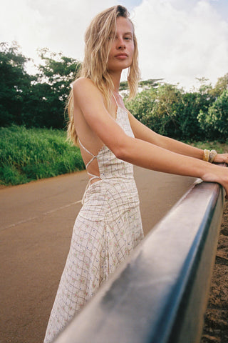 Woman in a white dress standing on a road with greenery in the background