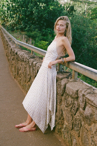 Woman in a white patterned dress standing on a stone path with greenery in the background