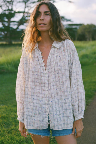 Woman wearing a plaid shirt and denim shorts standing in a grassy field.