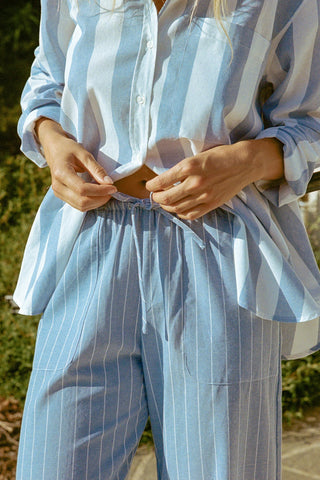 Person wearing light blue striped shirt and blue and white stripe pants outdoors