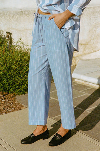 Person wearing light blue pinstripe pants and a white and blue stripe shirt outdoors.