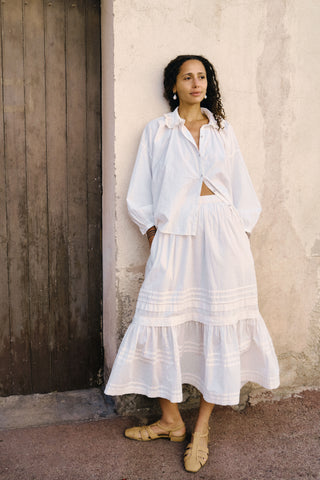 Woman in a white outfit standing against a textured wall.
