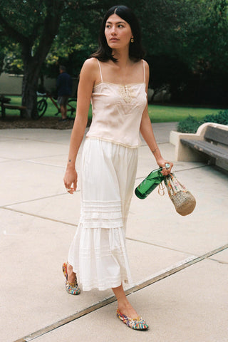 Women walking in a white skirt holding a bag and green bottle 