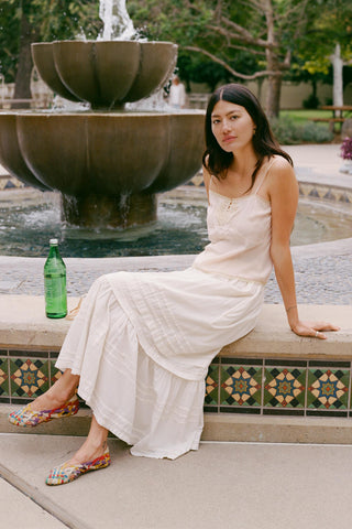 Women sitting in a white skirt with a green bottle with fountain behind her