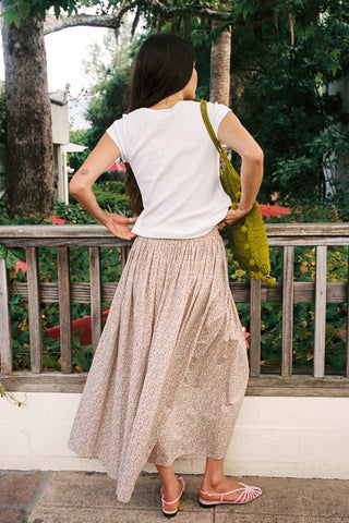 Back shot of a woman in a floral skirt and white tshirt with a bag over her shoulder