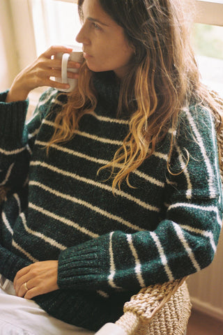 Woman wearing a green and white striped sweater, sitting indoors holding a mug.