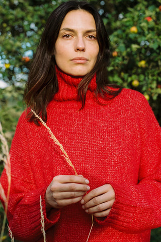 Woman wearing a red turtleneck sweater against an apple orchard holding long straw