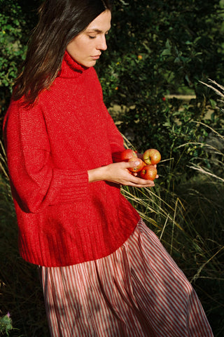 Woman in a red turtleneck sweater holding apples in a natural setting