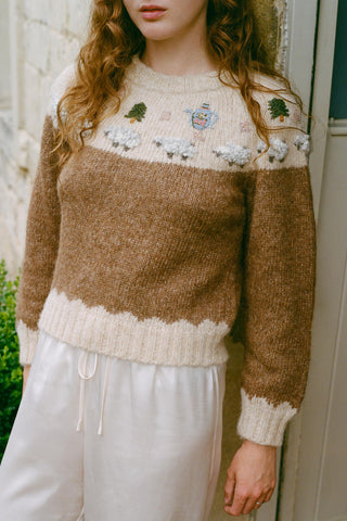 Person wearing a brown and beige sweater with floral patterns indoors.
