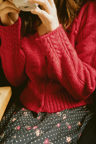 Person wearing a red knitted sweater and black pattern skirt with a blurred background