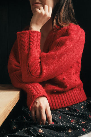 Person wearing a red knitted sweater with a dark background