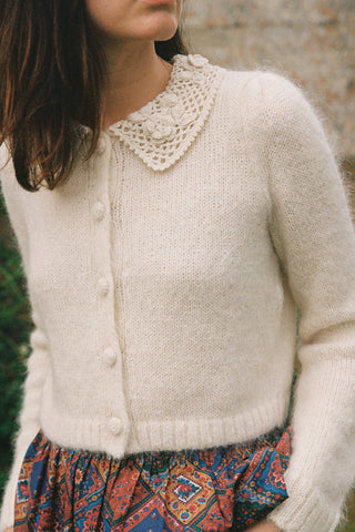 Person wearing a cream knitted cardigan with a decorative collar against a natural background