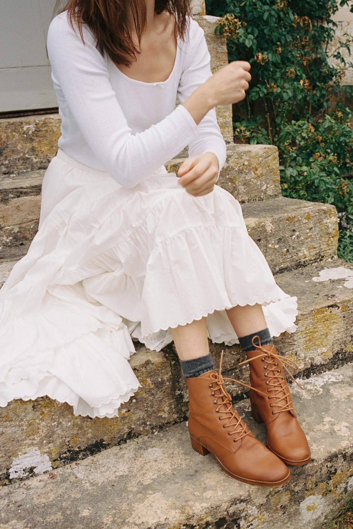 Camel-brown leather lace-up boots worn with a pale tiered skirt on old stone steps