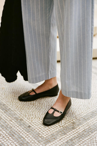 Person wearing black flats and light gray striped pants on a mosaic floor.